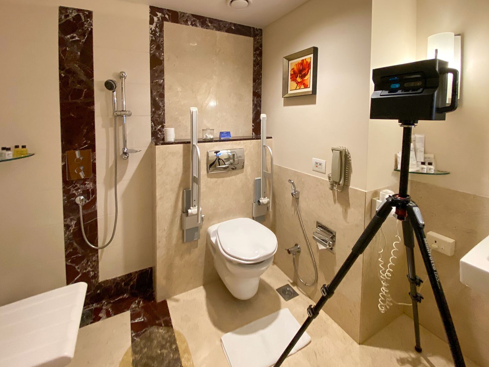 A well-equipped accessible hotel bathroom showing grab bars, a shower seat, and a roll-in shower.