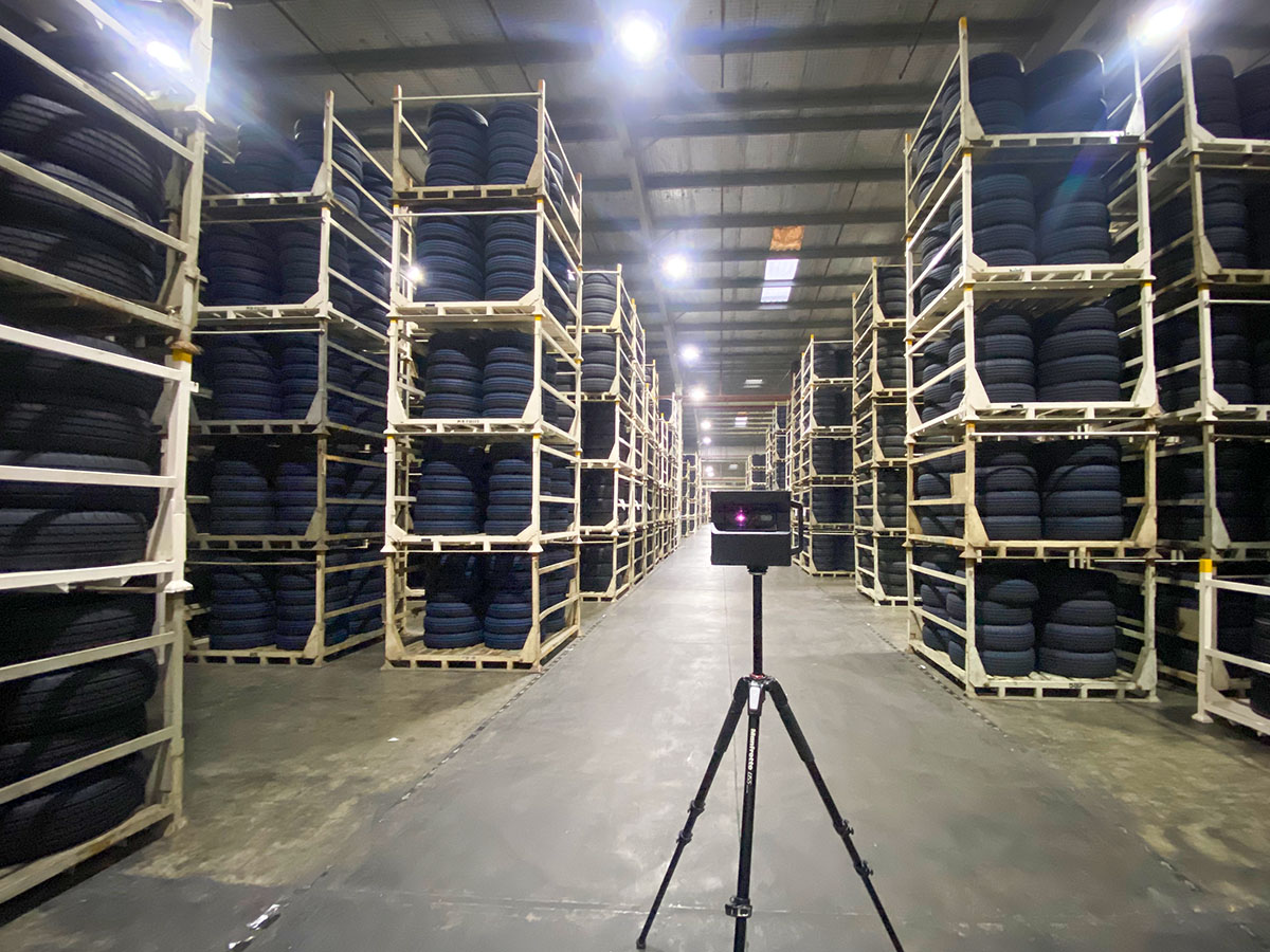 Large warehouse aisle flanked by tall multi-tiered storage racks loaded with finished tyres.