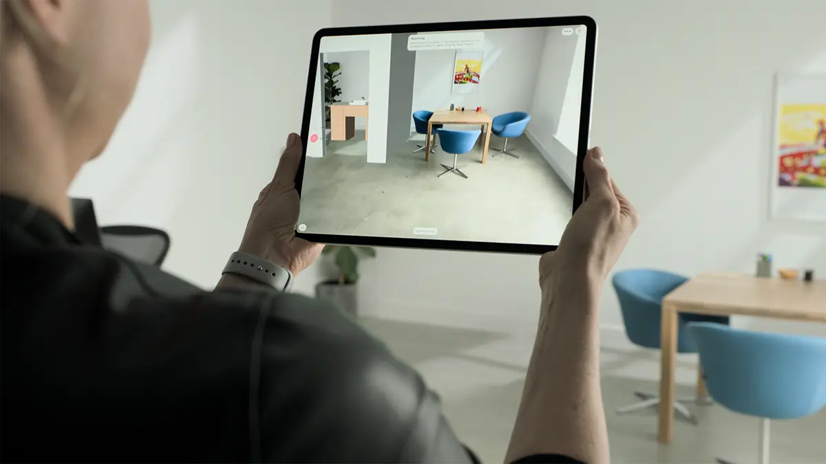 An Apple iPad Pro held horizontally, with a glowing blue LiDAR sensor overlay scanning a detailed university library interior.