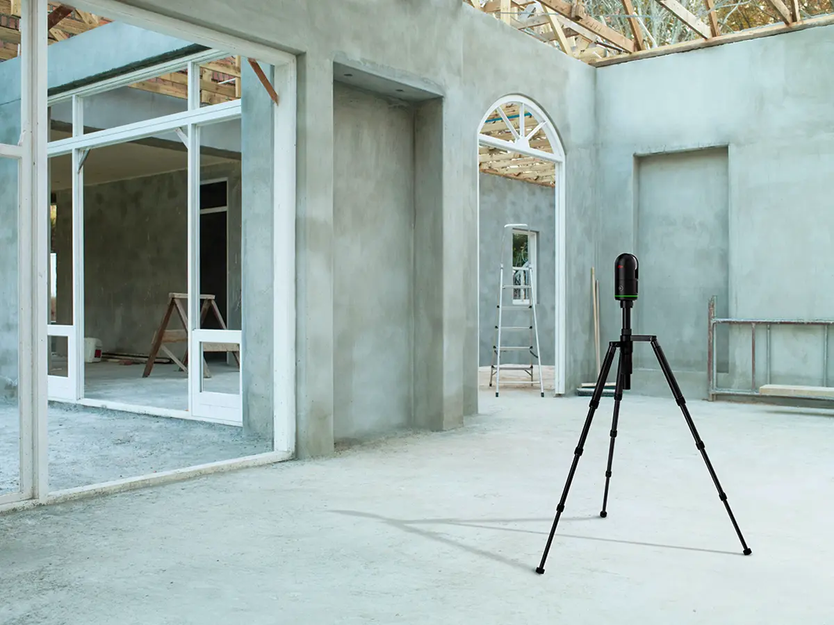 The sleek, black Leica BLK360 G2 laser scanner mounted on a tripod inside a modern, industrial building with concrete walls.