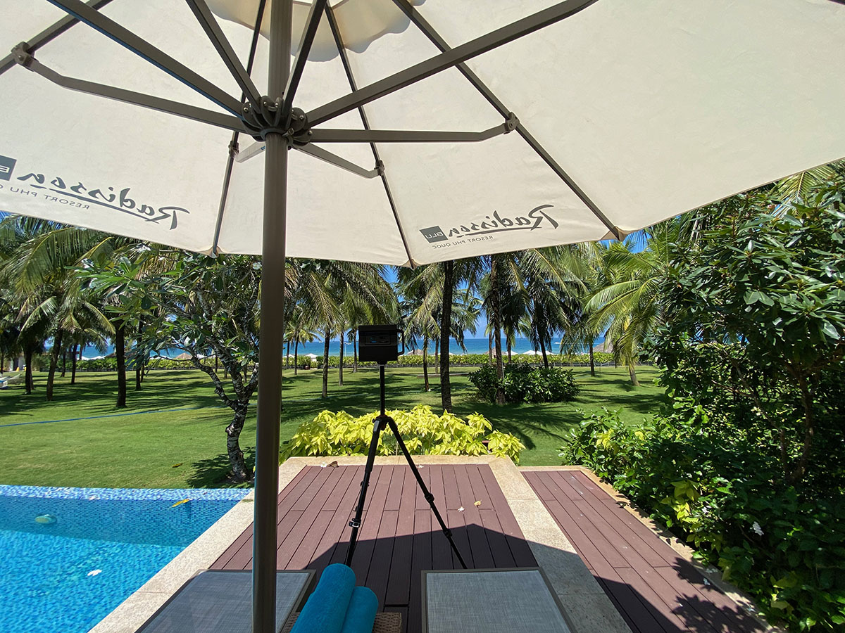 A 3D scanning camera positioned under a Radisson Blu branded patio umbrella, capturing the tropical beachfront and pool area.