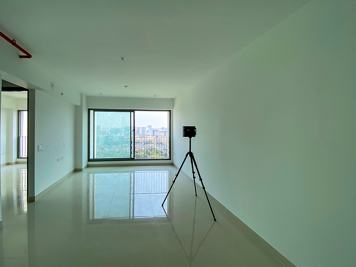 A Matterport Pro2 camera on a tripod scanning the interior of a modern apartment in Goregaon, Mumbai, with the city skyline visible through the window.