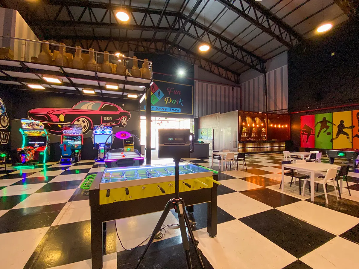 A professional-grade Matterport Pro2 camera on a tripod capturing a 3D scan of a gaming arcade with bright, colorful neon lights.
